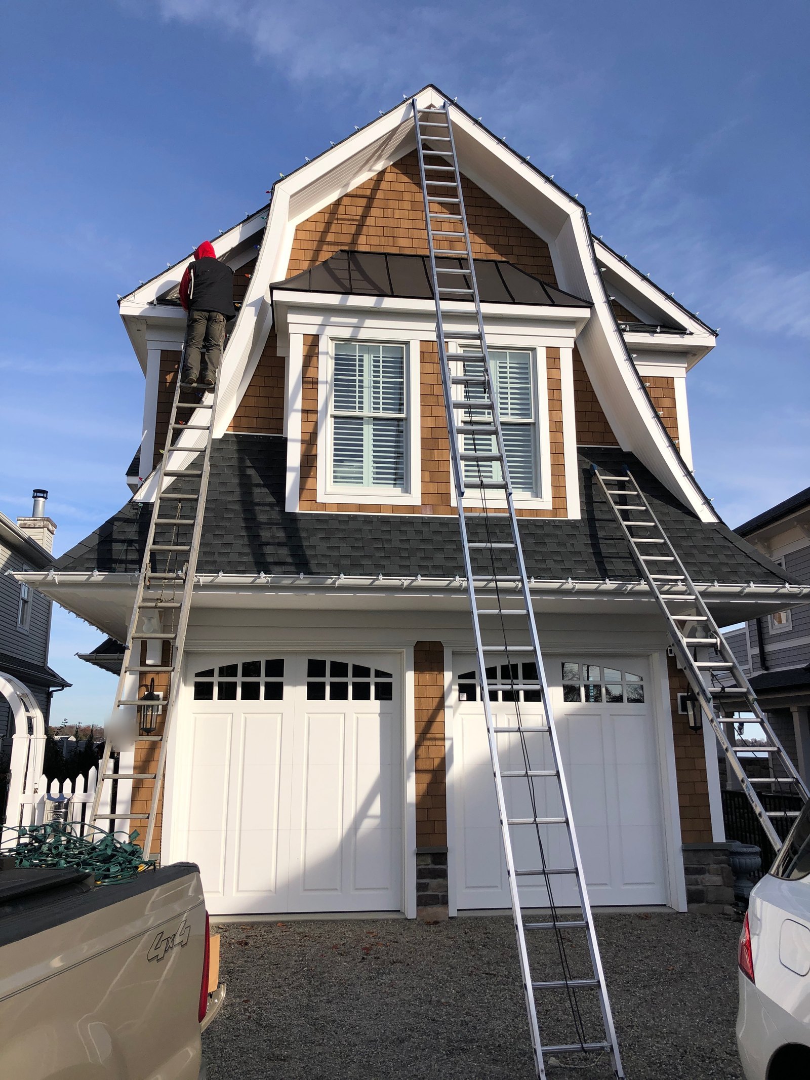 A+ Lighting technician installing Christmas lights with extension ladders on a tall New Jersey home